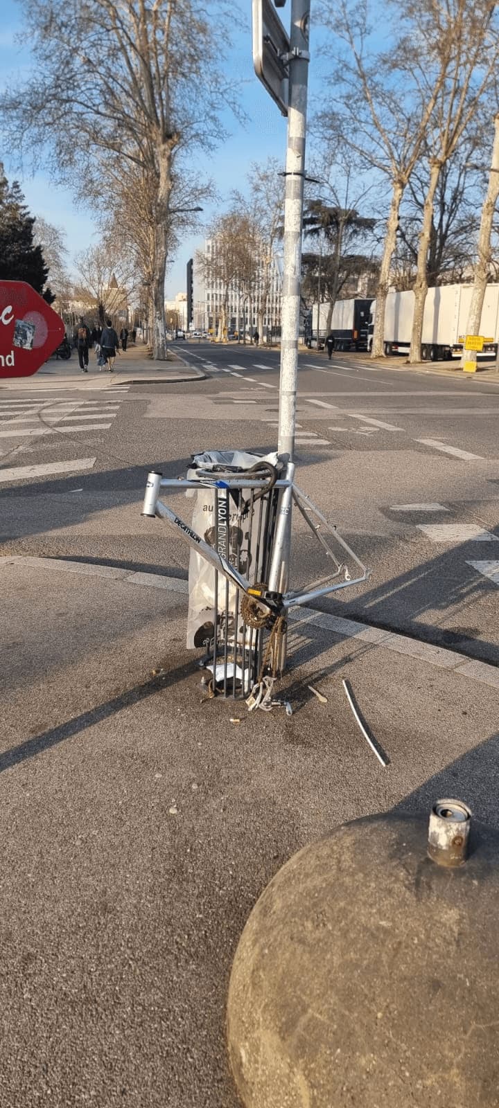 Cadre de vélo dépouillé de ses roues et de ses composants, resté cadenassé à un poteau dans une rue