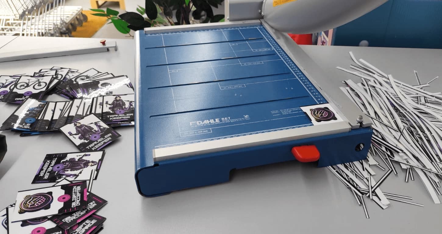 Massicot sur une table, entouré des cartes du jeu plastifiées et des chutes de découpe