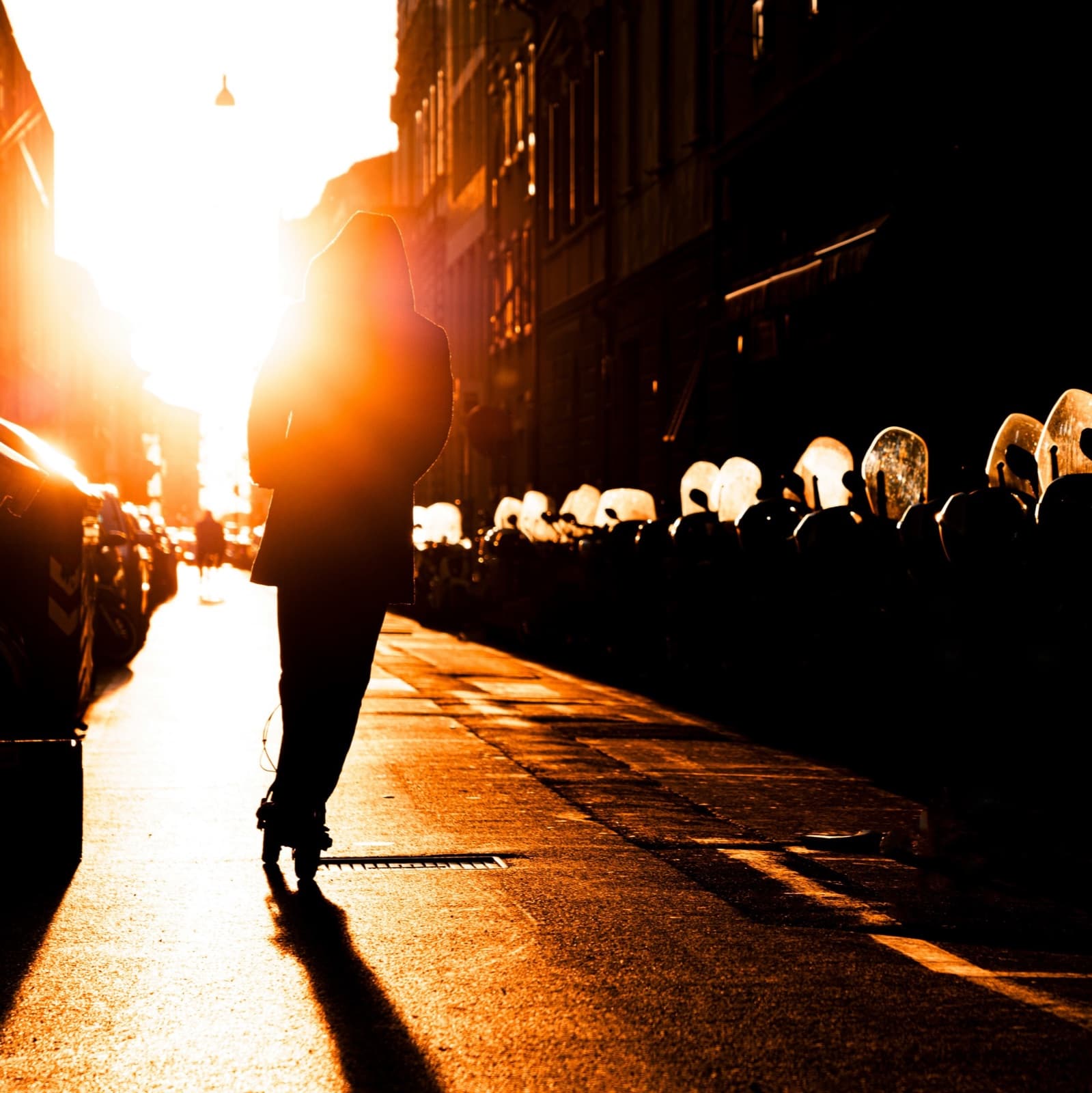 Silhouette d’une personne sur une trottinette, à contre-jour dans une rue au soleil couchant