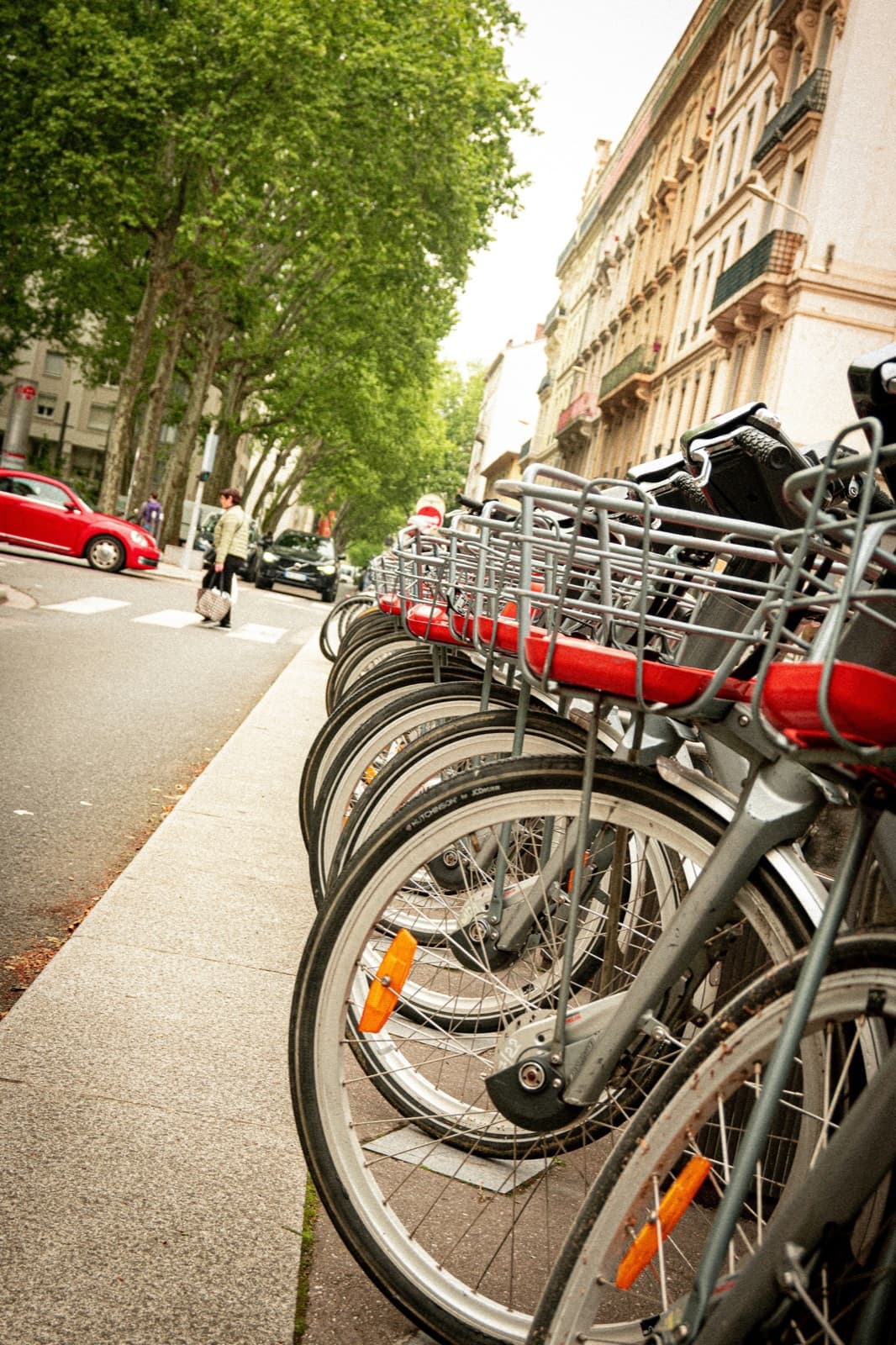 Rangée de vélos en libre-service alignés le long d’un trottoir, dans une avenue arborée