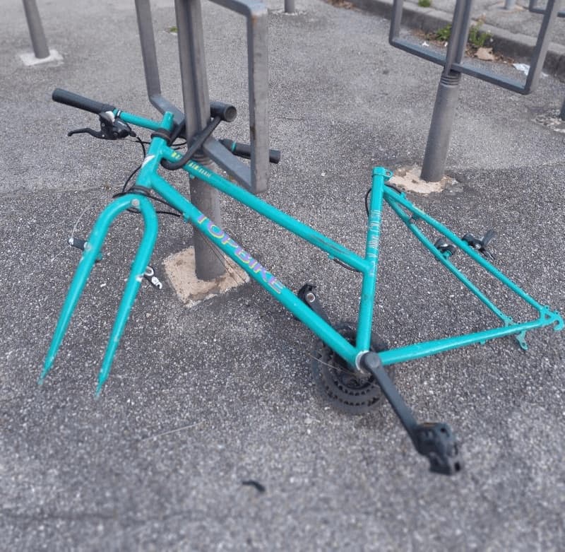 Cadre de vélo turquoise dépouillé de ses roues, resté attaché à un arceau de stationnement