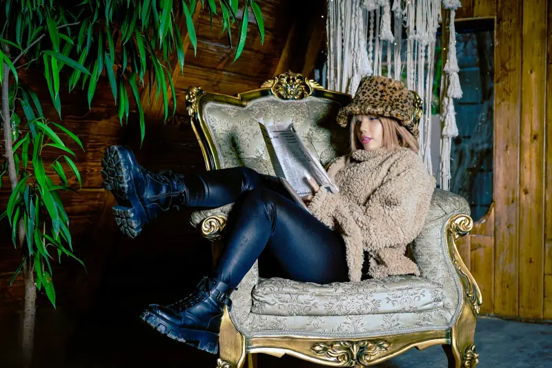 Une jeune femme en toque de fourrure lit, installée dans un fauteuil baroque doré